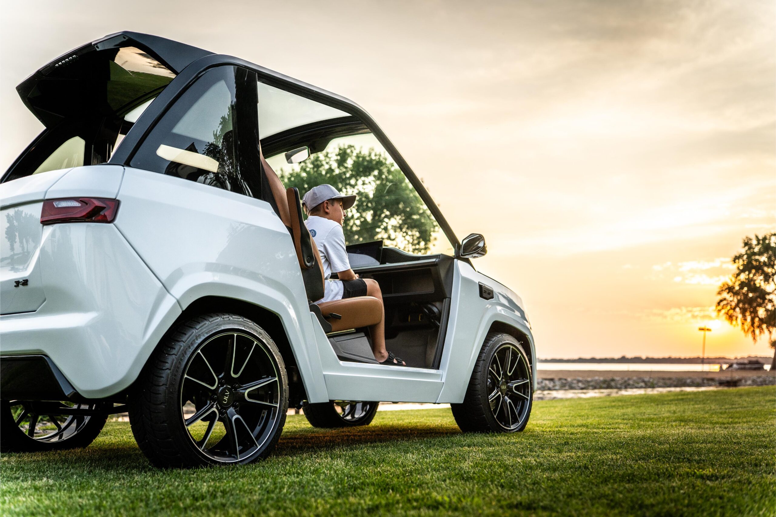 a young boy looks out at a sunset over a lake from the passenger's seat of a white ulv model